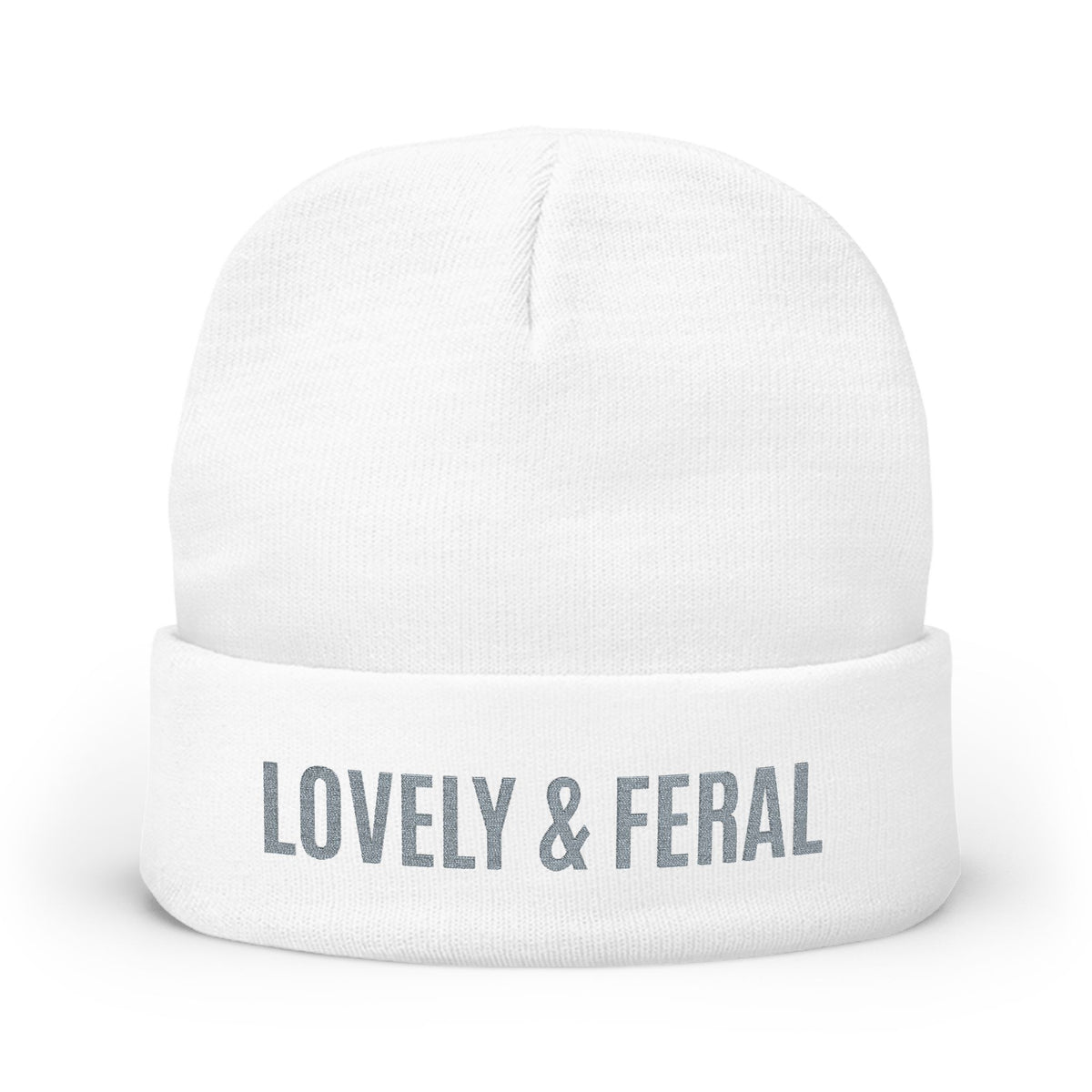 A white knit cuffed beanie hat with the words 'LOVELY & FERAL' printed in gray on the front cuff, shown against a plain white background.